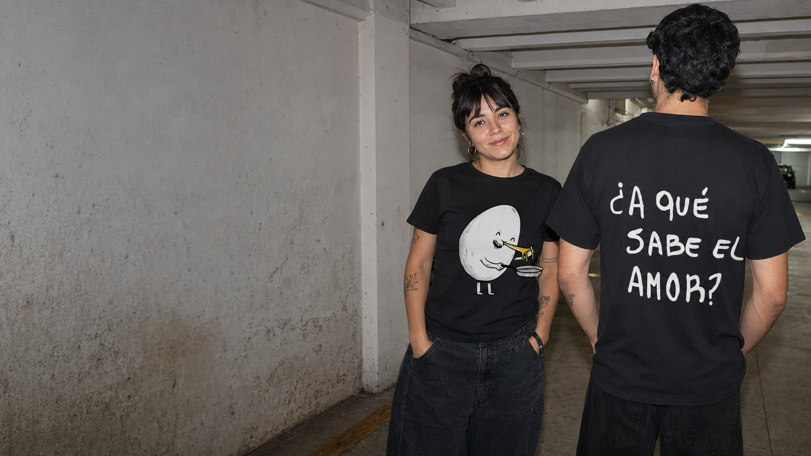 Dos personas con remeras negras personalizadas de Devrim en un estacionamiento.