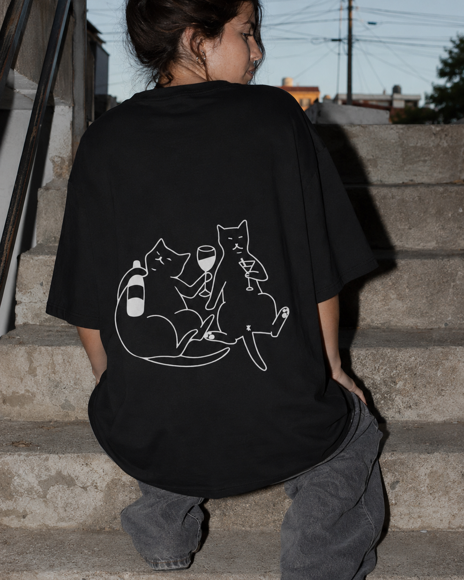 Remera oversize negra con ilustración lineal de dos gatos en la espalda.